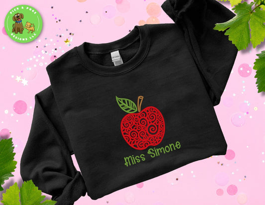Black Gildan crewneck style crewneck with embroidered swirl apple design and teacher name under the apple.